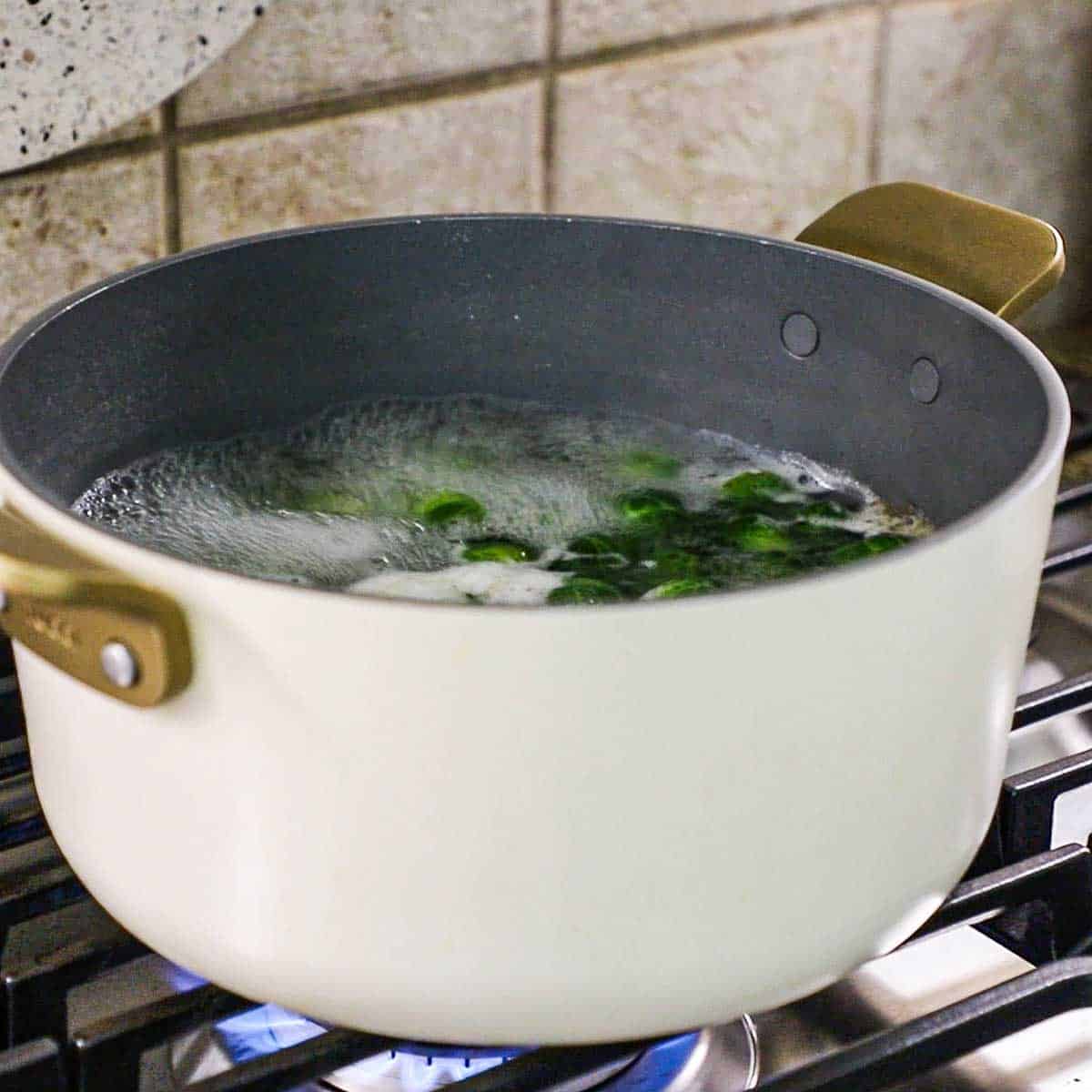 A large pot of boiling water on a gas stove filled with simmering Brussels sprouts.