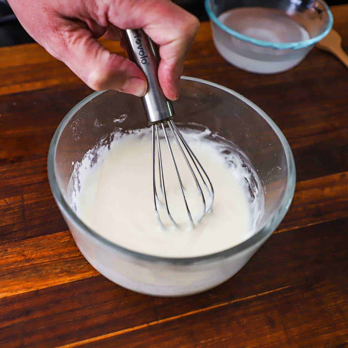 A person using a small whisk to combine powder sugar with heavy cream and vanilla extract to create a glaze.