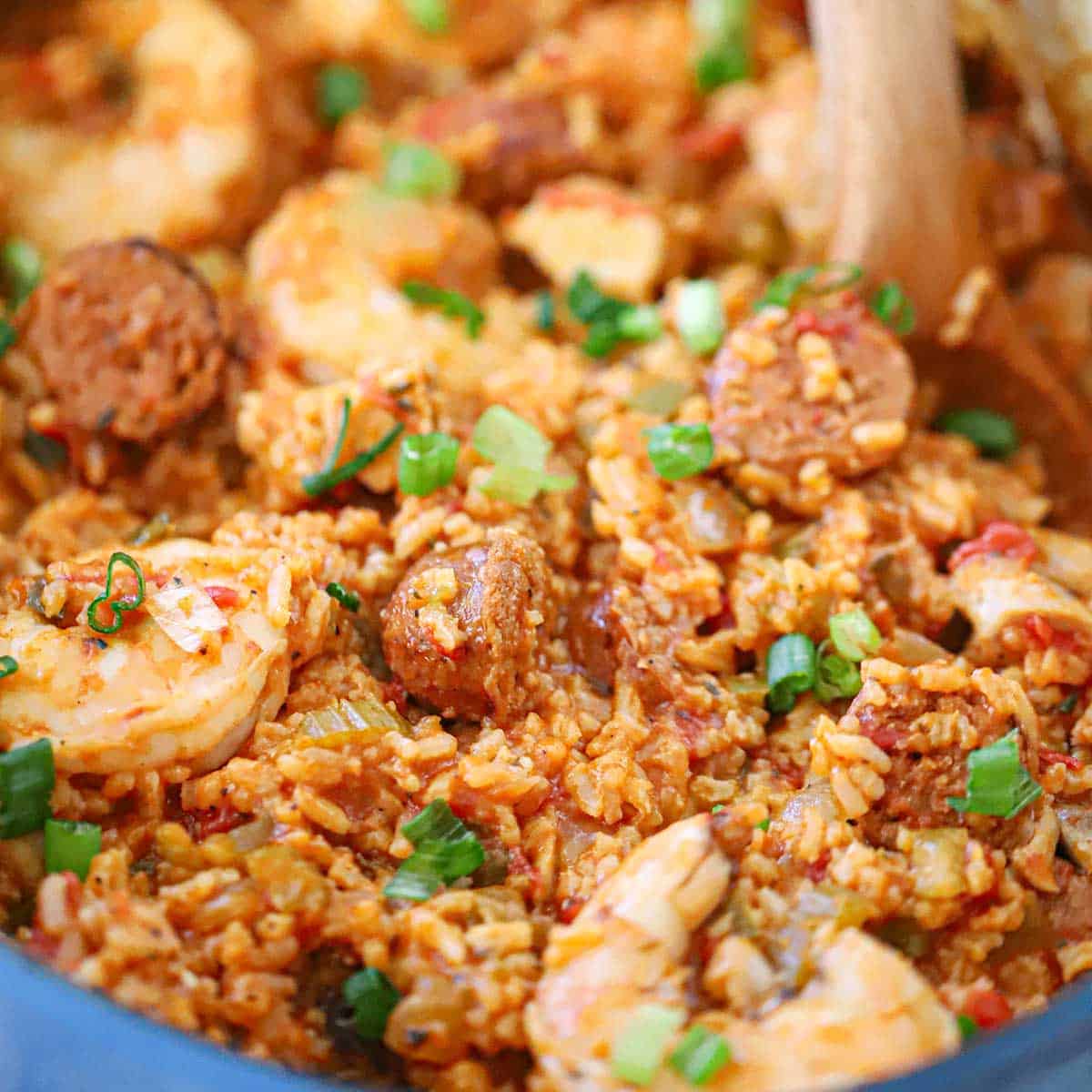 A close-up view of a wooden spoon being used to stir a fresh prepared vat of authentic jambalaya in a large Dutch oven.