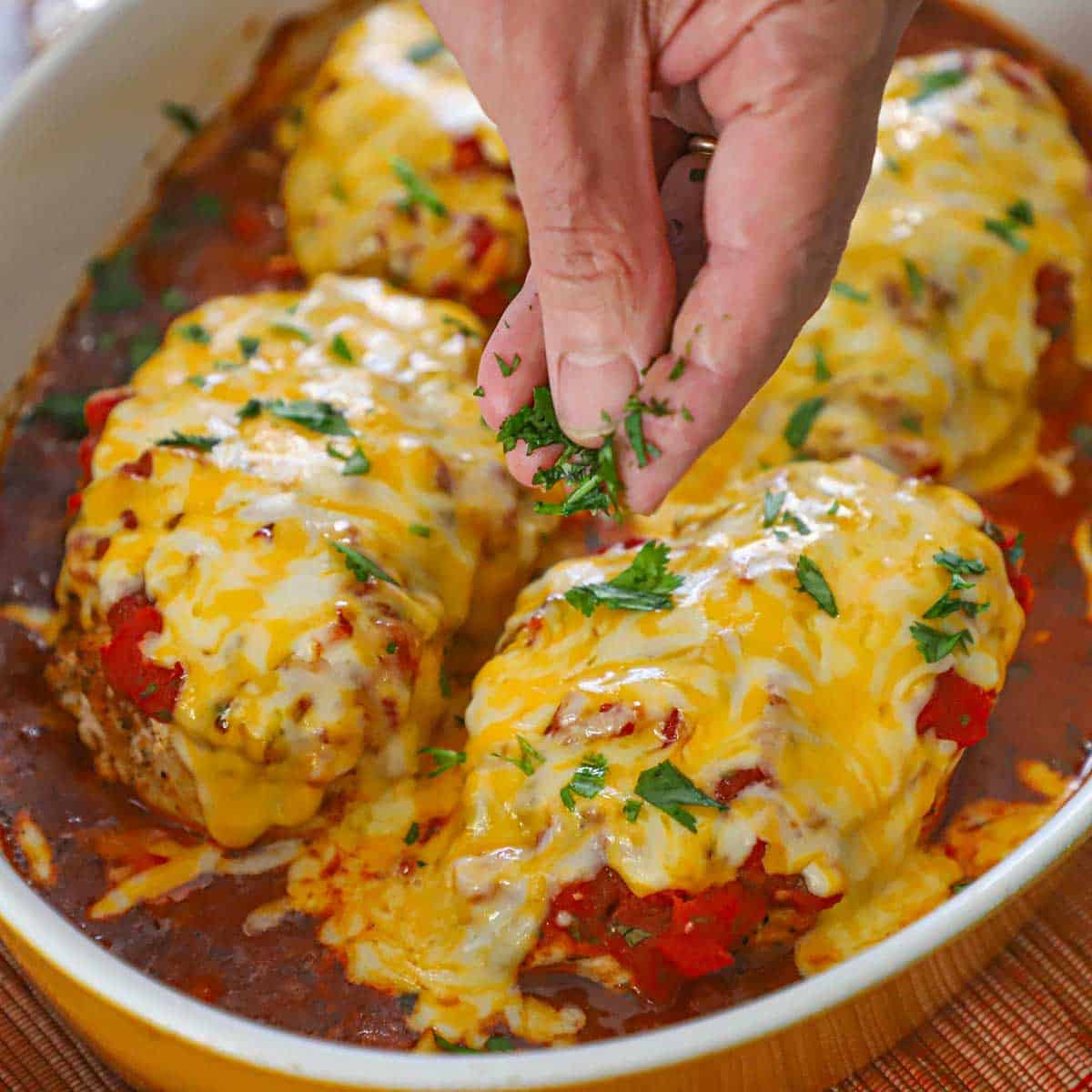 A person sprinkling chopped cilantro over the tops of freshly baked cheesy salsa chicken in a large casserole dish.