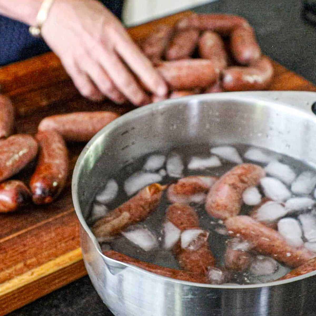 A person using his hands to place links of freshly smoked Texas Jalapeño Cheddar Sausage into a large metal bowl filled with ice water.