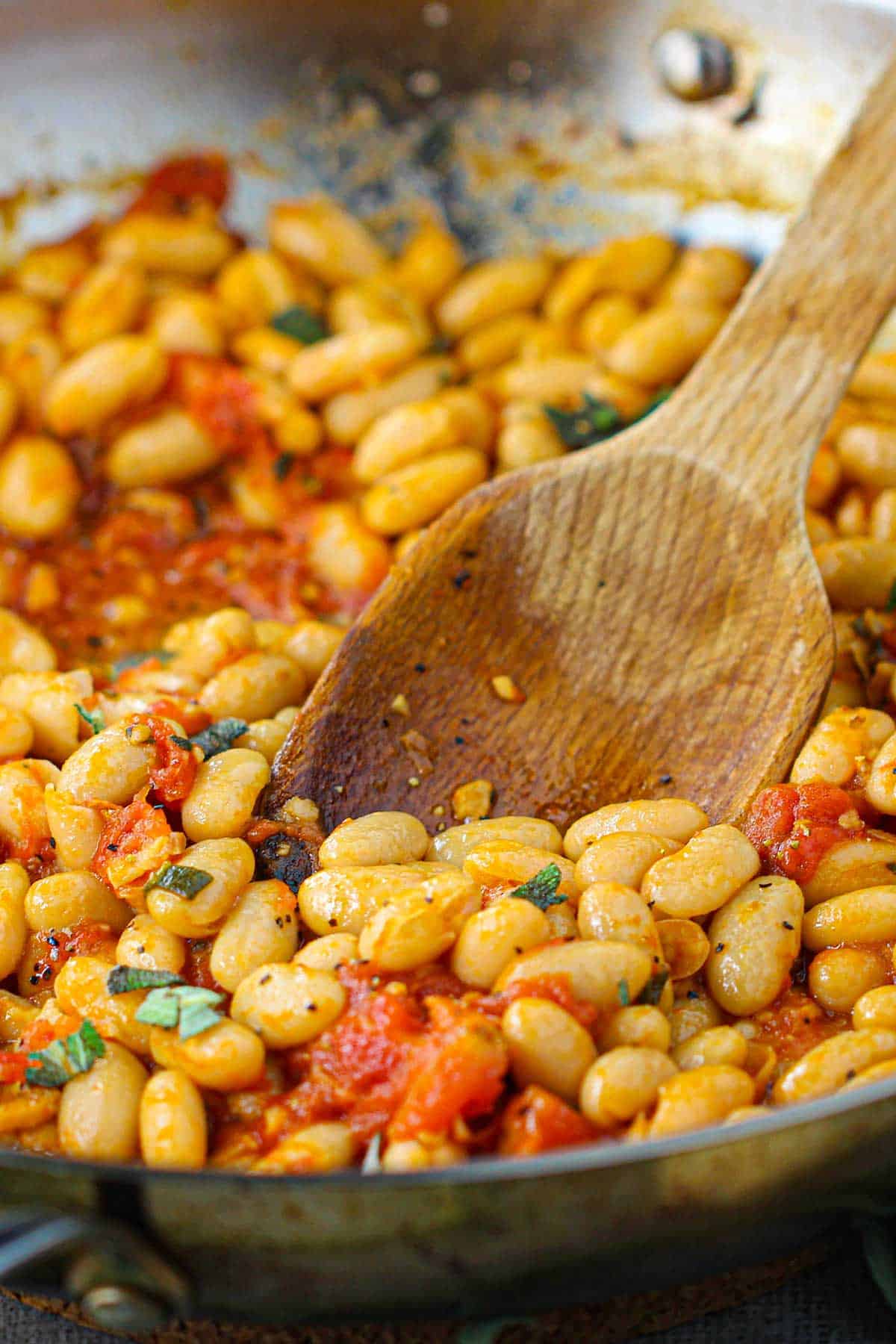 A straight-on view of a large silver skillet filled with freshly prepare Saut&eacute;ed White Beans with Garlic, Sage, and Tomatoes.