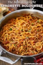 A straight-on view of a large skillet that is filled with spaghetti bolognese that is garnished with chopped Italian parsley.