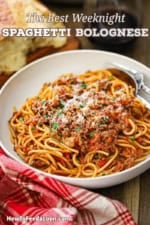 A straight-on view of a shallow white pasta bowl filled with a serving of pasta bolognese next to a stemless glass of red wine.