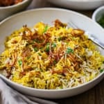 A straight-on view of a shallow bowl filled with a serving of Hyderabadi Chicken Biryani topped with fried onions and chopped cilantro.
