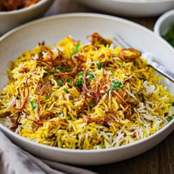 A straight-on view of a shallow bowl filled with a serving of Hyderabadi Chicken Biryani topped with fried onions and chopped cilantro.