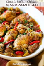 A straight-on view of a large oval platter filled with Crispy Chicken Scarpariello consisting of seared chicken legs and thighs with chunks of Italian sausage all resting in a bell pepper and cherry pepper brown sauce.