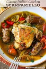 A close-up view of a shallow bowl filled with a serving of Chicken Scarpariello recipe with a crispy chicken thigh and several pieces of cooked Italian sausage in a pepper and onion broth.