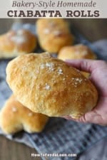 A person holding a large bakery-style homemade ciabatta roll in the palm of his hand.
