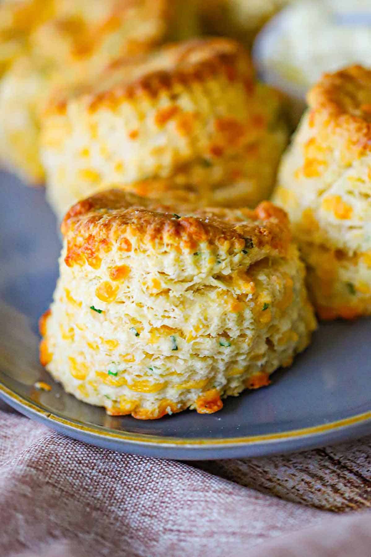 A close-up view of flaky cheddar biscuits sitting in a row on an oval grey platter with a small bowl of softened butter next to the biscuits.