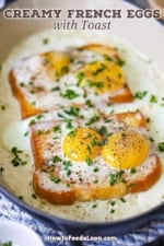 A straight-on view of French Baked Eggs with Cream in an oval baking dish topped with snipped chives two glass mugs of coffee and a large silver serving spoon resting nearby.