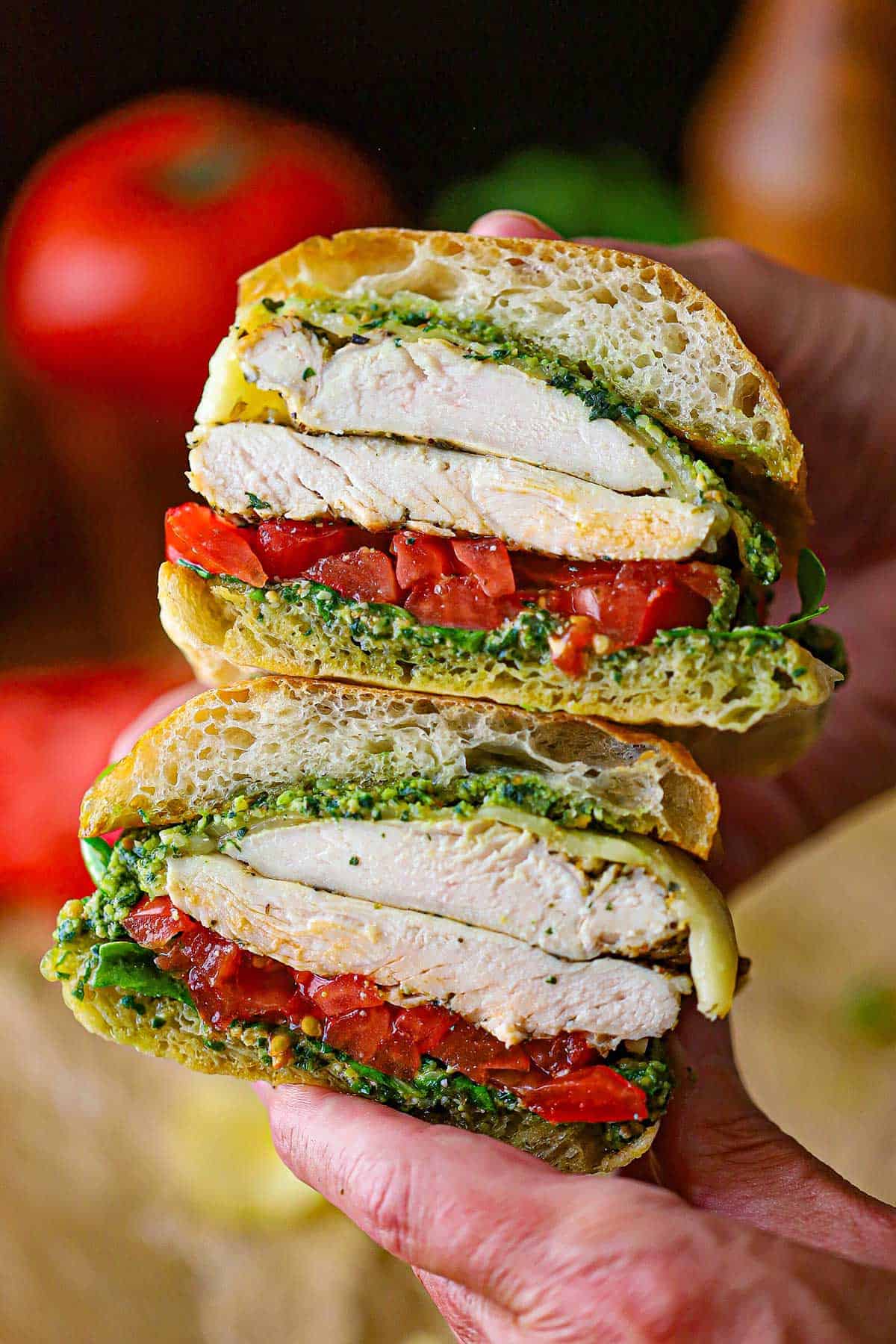 Two halves of Grilled Pesto Chicken Sandwich that a person is holding top of each other revealing the layers within the sandwich.