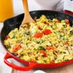 A close-up view of a large skillet with a red base filled with an Italian Skillet Scramble topped with blistered cherry tomatoes and chopped basil.