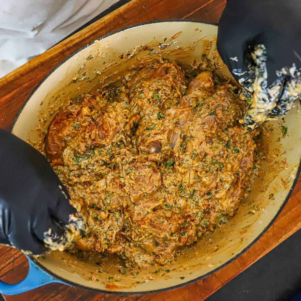 A person wearing black kitchen gloves massaging chicken pieces in a creamy, seasoned marinade for chicken biryani.