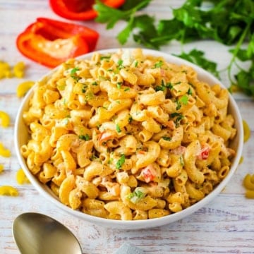 A close-up view of a shallow white bowl filled with freshly prepared Cajun pasta salad and garnished with chopped parsley.