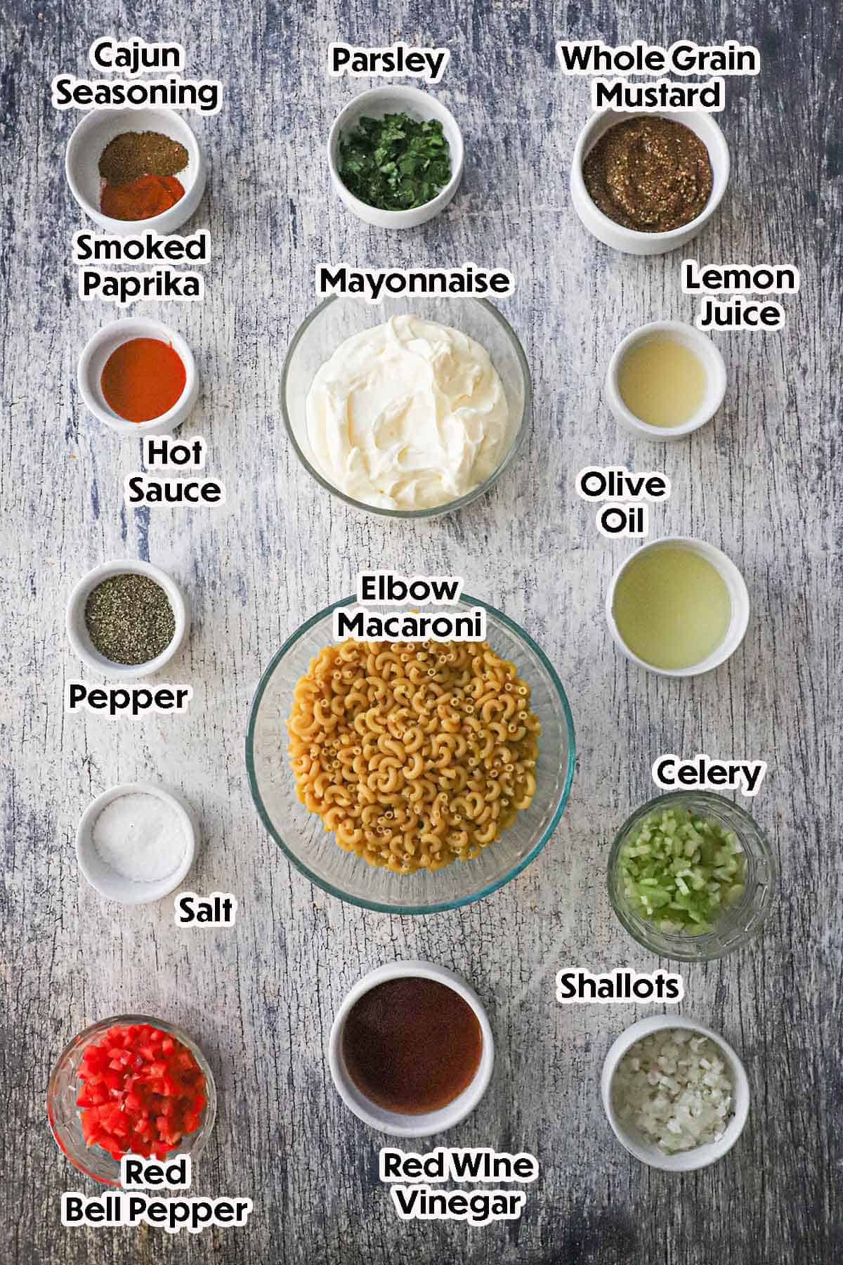 An arrangement of ingredients for Cajun Pasta Salad including elbow macaroni, mayonnaise, red bell pepper, celery, shallots, mustard, lemon juice, herbs, and seasonings.