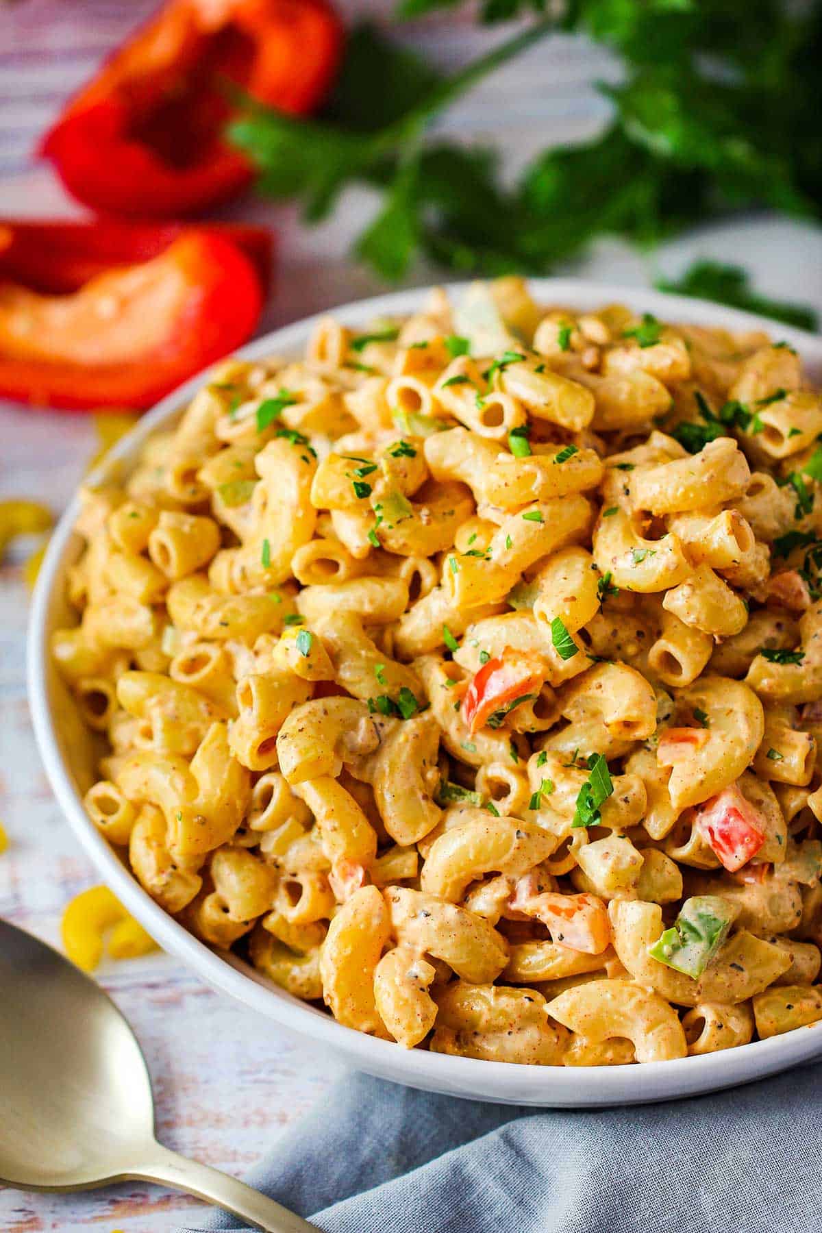 A close-up view of a shallow white bowl filled with freshly prepared Cajun pasta salad and garnished with chopped parsley.