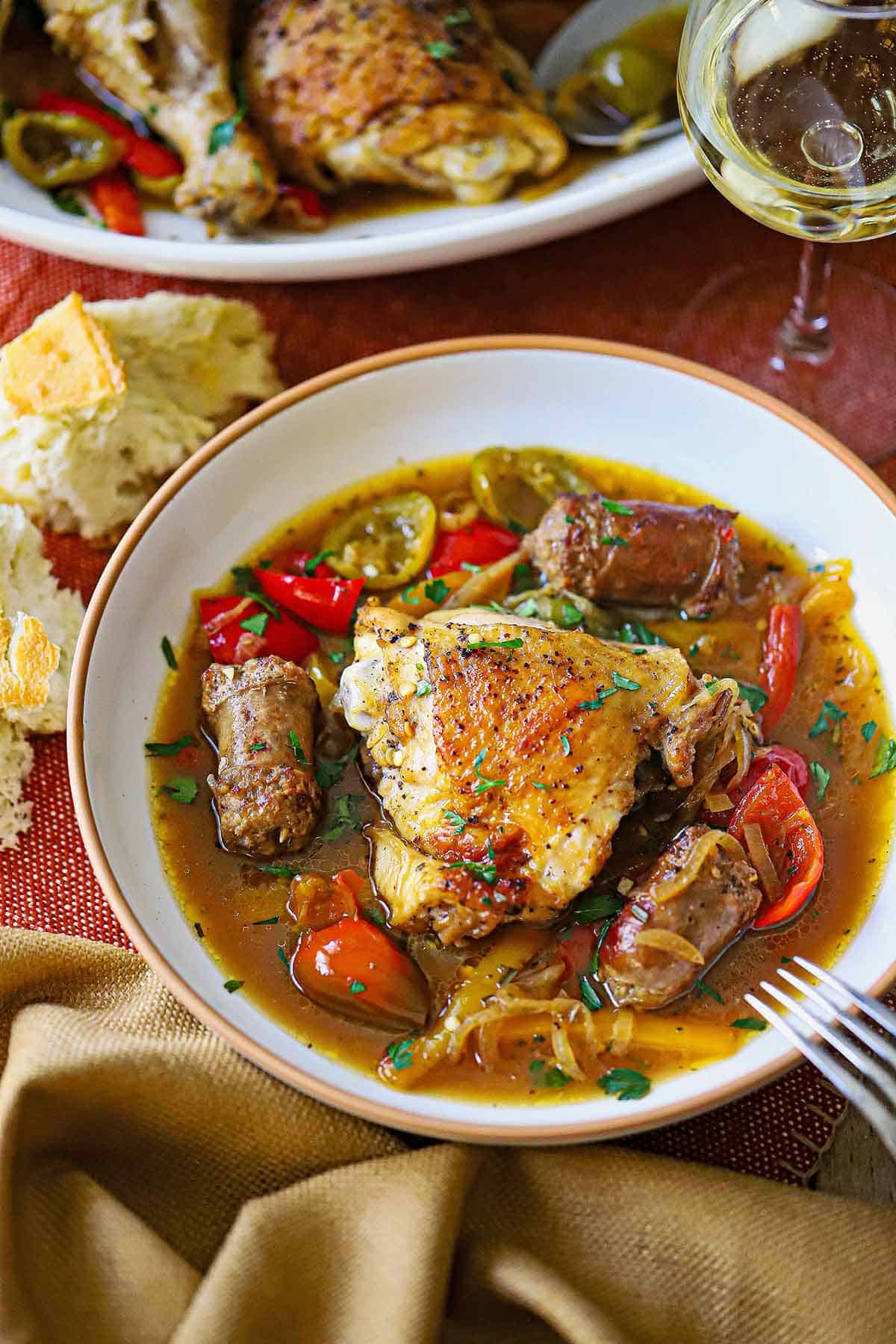 An overhead view of a shallow bowl filled with a serving of Chicken Scarpariello recipe with a crispy chicken thigh and several pieces of cooked Italian sausage in a pepper and onion broth.