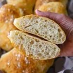 A close up view of two halves of a homemade ciabatta bun that has been split in half and the inside with large air pockets are visible and is being held in the palm of person's hand.