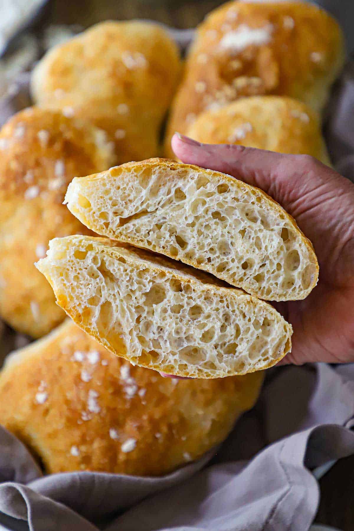 A person holding two halves of a homemade ciabatta bun that has been split in half and the inside with large air pockets are visible.
