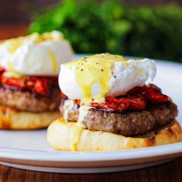 A close-up view of two servings of Eggs Blackstone with Sausage sitting side-by-side on a white dinner plater.