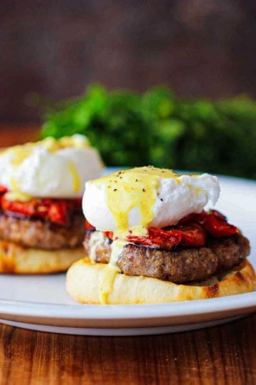 A straight-on view of two servings of Eggs Blackstone with Sausage sitting side-by-side on a white dinner plater.
