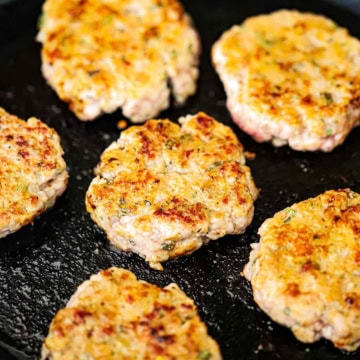 A close-up view of six maple sausage patties being cooked on a large black non-stick skillet.