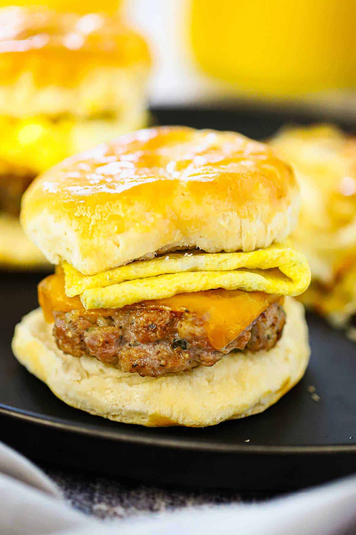 A straight-on view of a best-ever breakfast sandwich consisting of a maple sausage patty topped with melted cheddar cheese and a folded sheet of scrambled egg between a buttered biscuit.