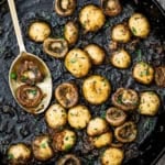 An overhead view of sautéed mushrooms in a large black cast-iron skillet and garnished with chopped Italian parsley.