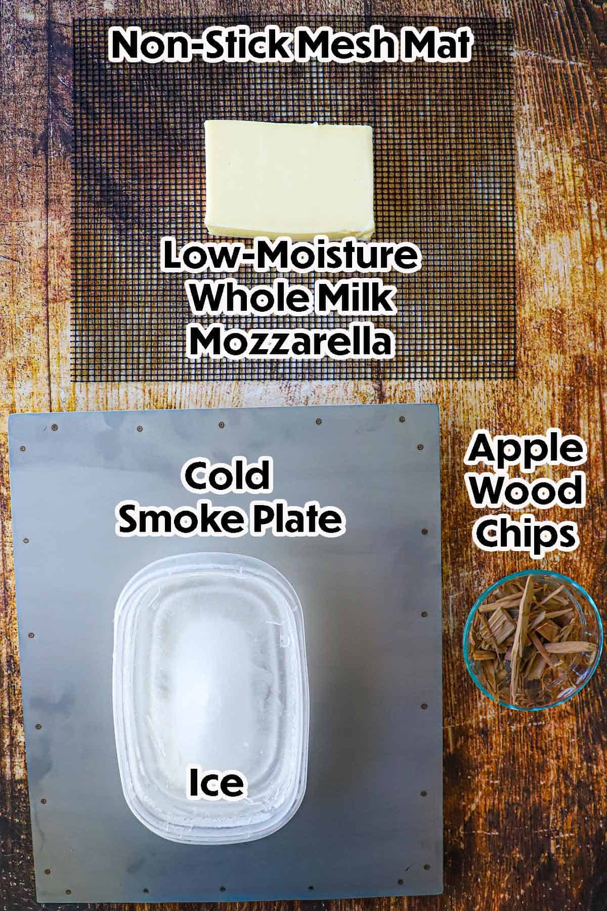 An arrangement of tools and ingredients for smoked mozzarella on a wooden background including a non-stick mesh mat, cold smoke plate, wood chips, a block of mozzarella, and a plastic container filled with ice.