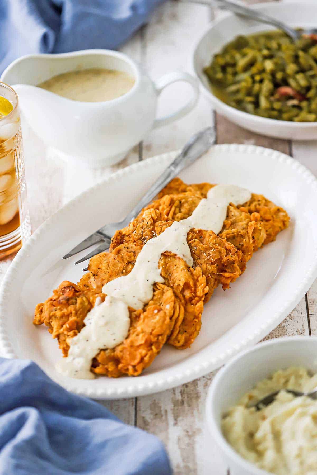 Four Southern-Fried Pork Chops stacked against each other on an oval platter with a row of cream gravy across the top center of each chop.