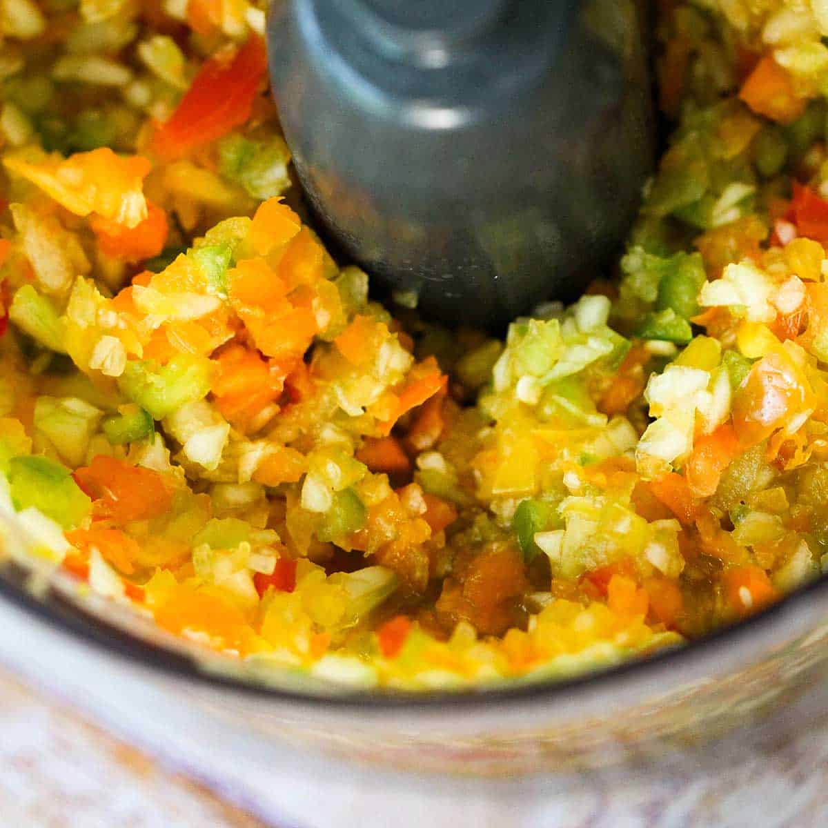 A close-up view of a food processor filled with finely chopped cucumber and bell peppers.