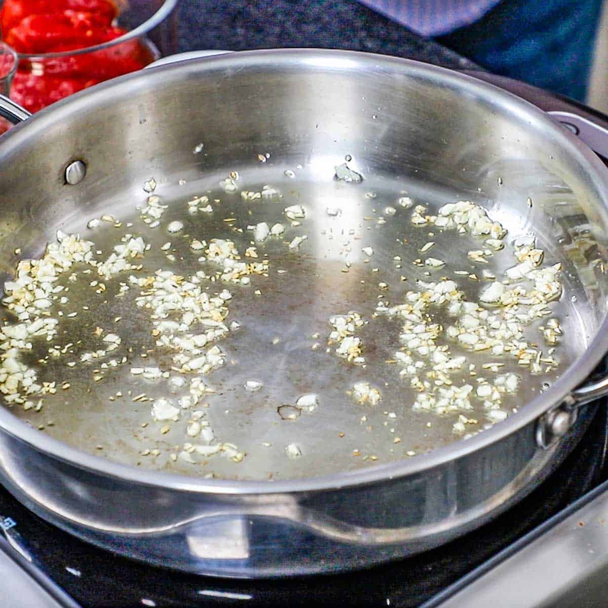 A large skillet filled with minced garlic simmering in oil on top of an induction oven.
