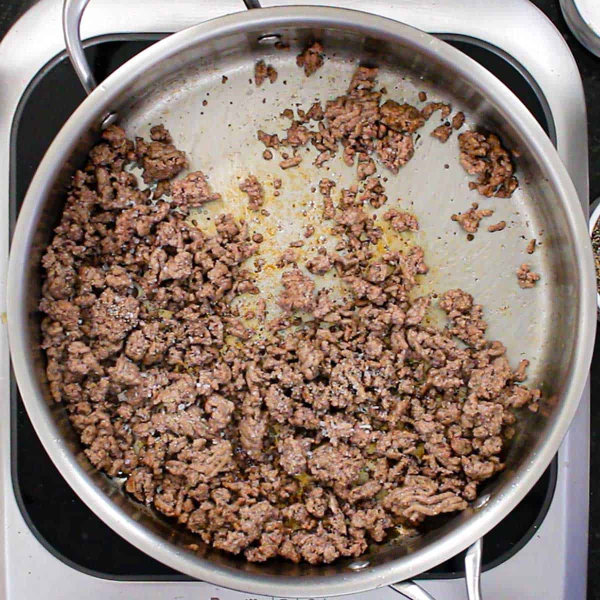 An overhead view of a large stainless steel skillet filled with cooked seasoned ground beef.