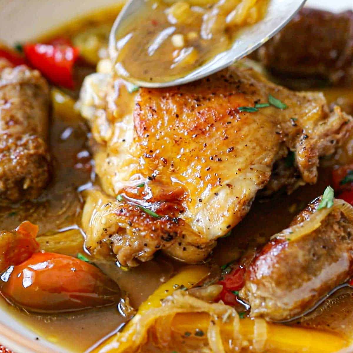 A large silver spoon being used to drizzle a sauce over the top of a seared chicken thigh resting in a bowl filled with chicken scarpariello sauce.