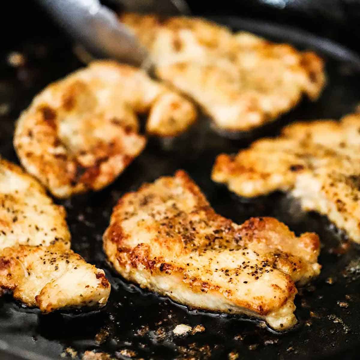 A close-up view of seasoned and floured slices of pork tenderloin being pan-fried in oil in a large cast-iron skillet.