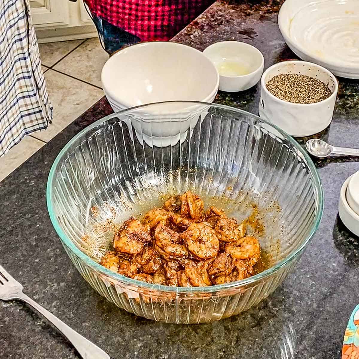 A large glass bowl filled with seasoned shrimp on a black marble countertop.