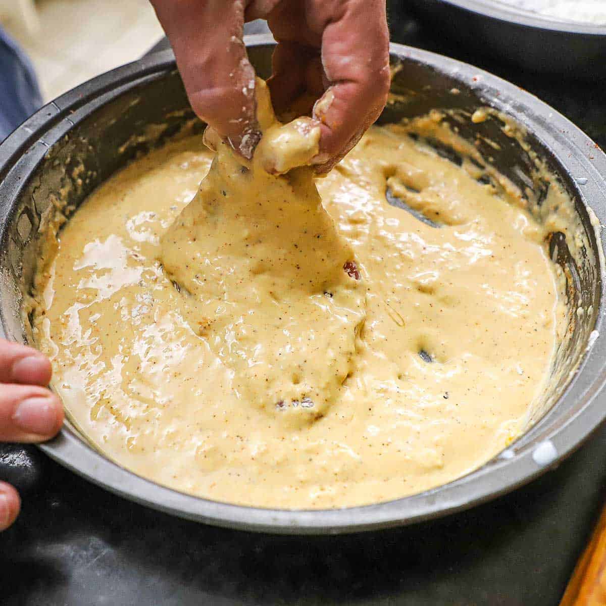 A person using his fingers to submerge a floured thin, boneless, pork chop in a wet batter for fried pork chops.