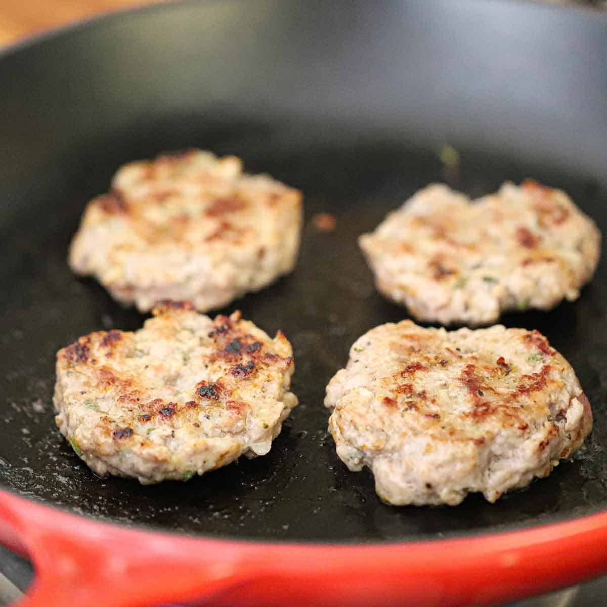 Four maple sausage patties being cooked and seared in a large non-stick skillet.