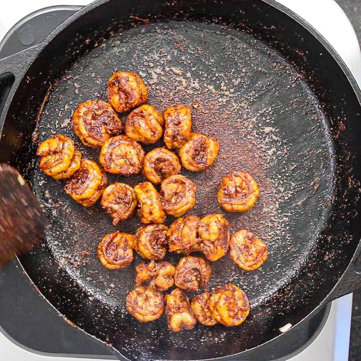 An overhead view of seasoned shrimp that is being cooked and blackened in a large cast-iron skillet.