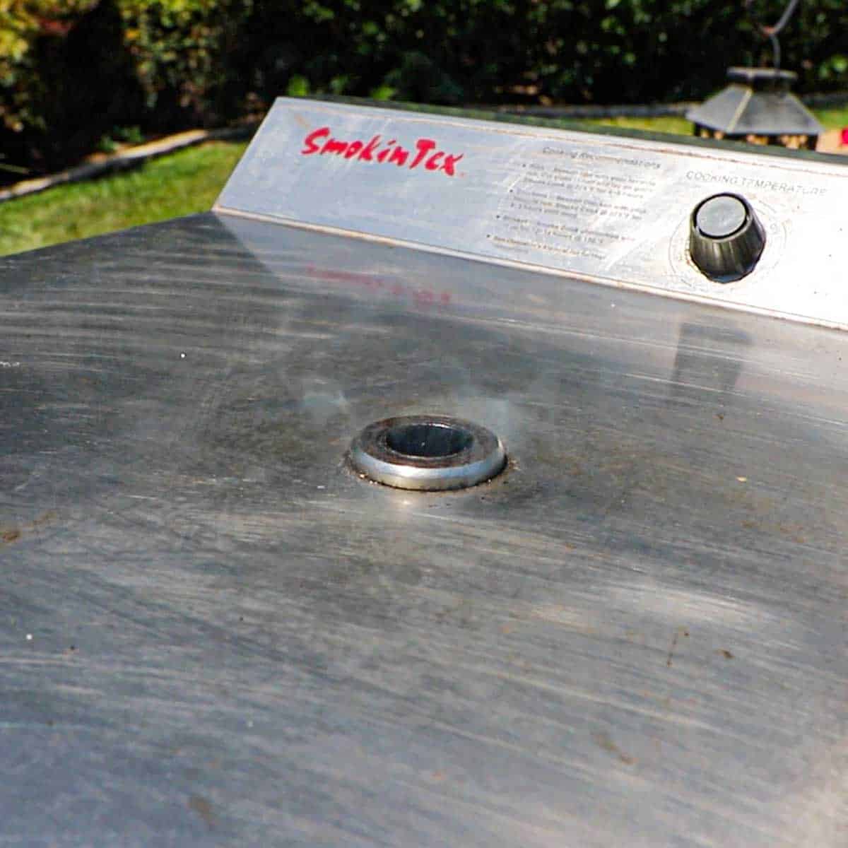 A close-up view of smoke billowing out of a whole in the top of an electric smoker.
