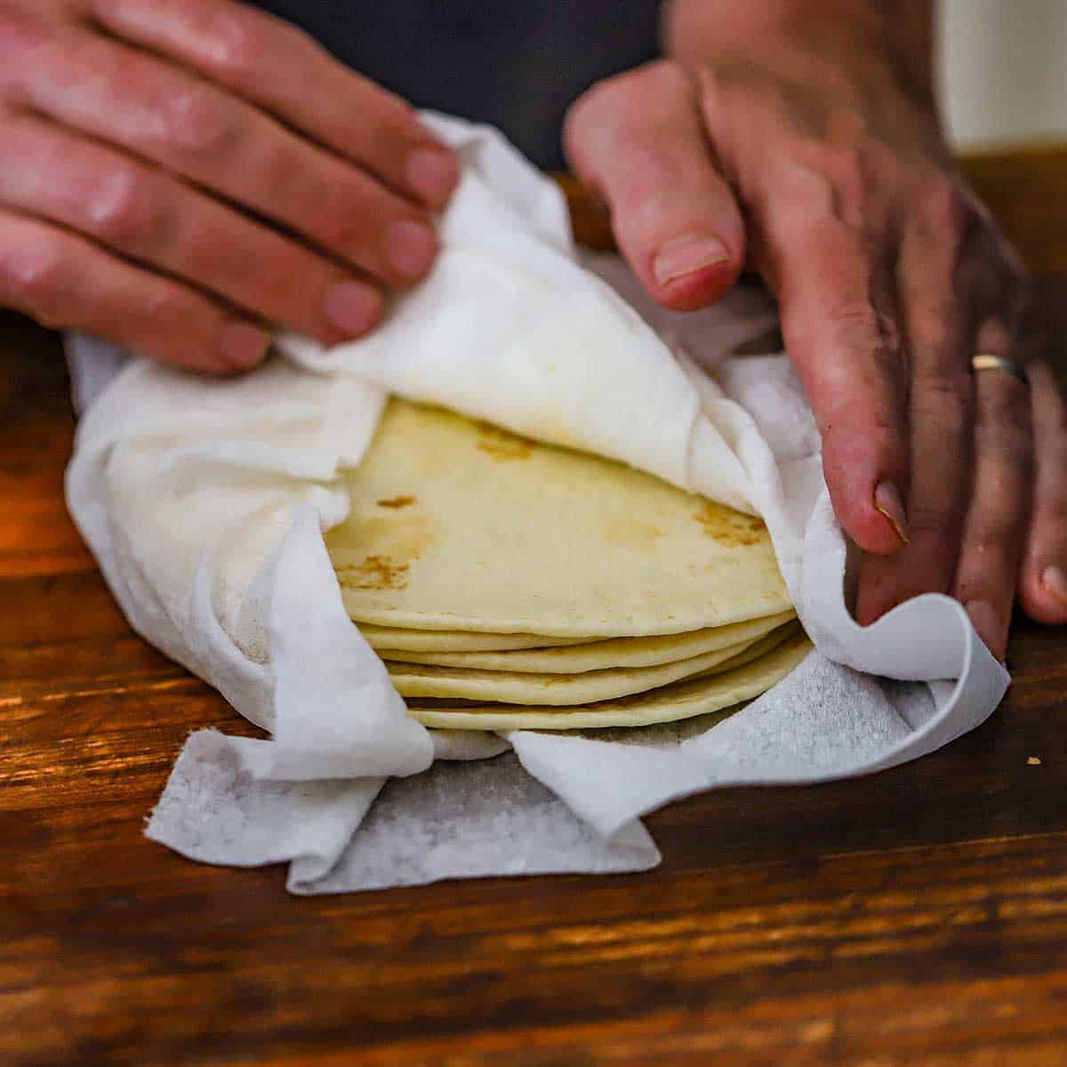 A person pulling back paper towels that have been wrapped around a stack of flour tortillas that have been warmed in a microwave.