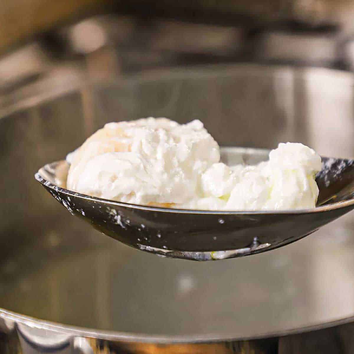 A slotted spoon being used to raise a poached egg from a pot of hot, steaming water.