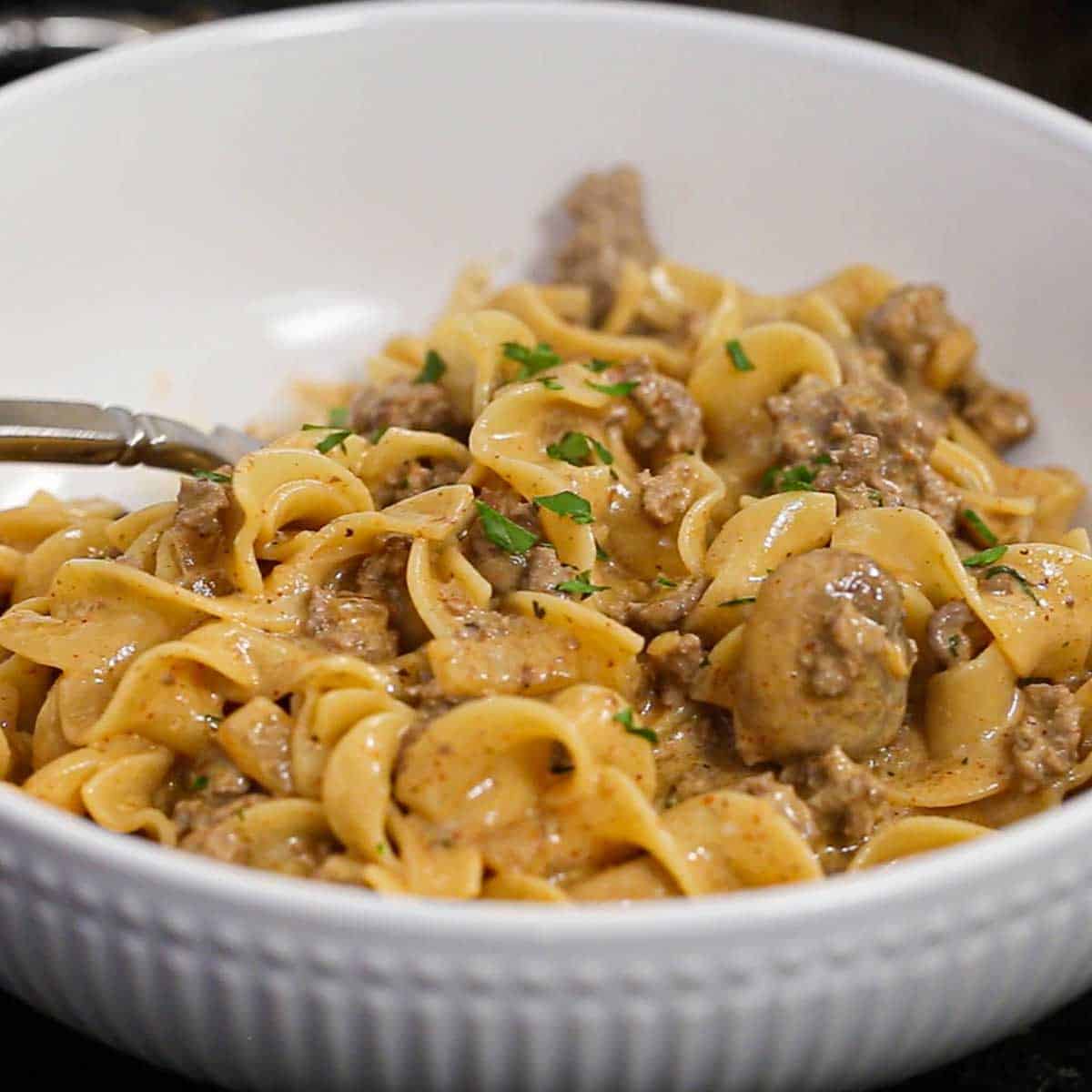 A close-up view of a white pasta bowl filled with a serving of Weeknight Beef Stroganoff garnished with chopped Italian parsley.