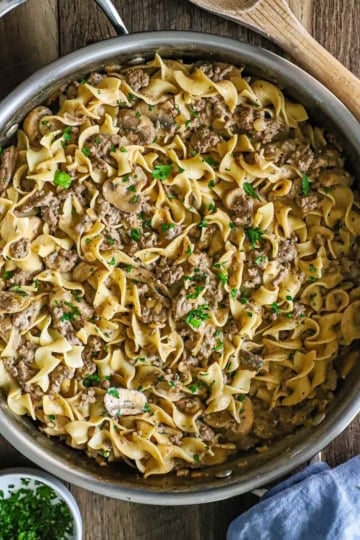 An overhead view of a large skillet filled with Weeknight Beef Stroganoff that is topped with finely chopped Italian parsley.