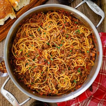 An overhead view of a large skillet that is filled with spaghetti bolognese that is garnished with chopped Italian parsley.