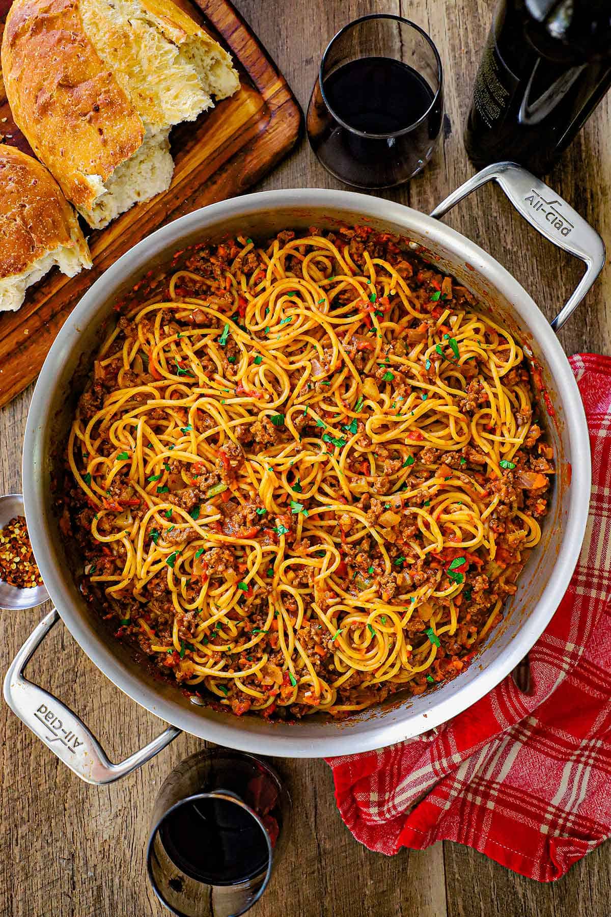 An overhead view of a large skillet that is filled with spaghetti bolognese that is garnished with chopped Italian parsley.