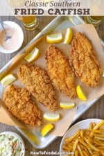 An overhead view of a large baking pan lined with brown paper and topped with four Southern fried catfish filets with lemon wedges around the sides of the pan along with bowls of French fries, coleslaw, and a Cajun remoulade near the pan.