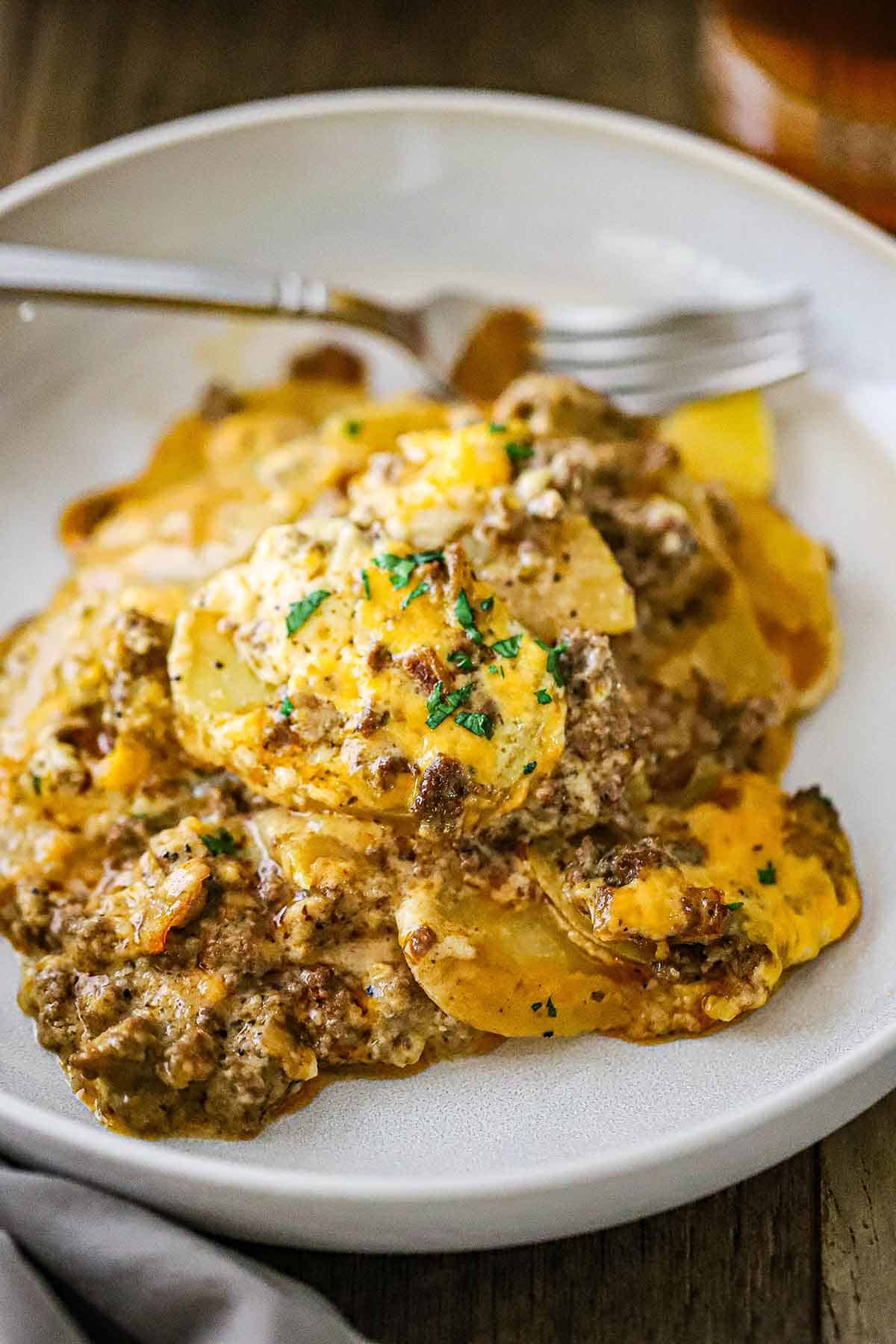 A serving of hamburger potato casserole piled high in a shallow bowl with a fork in the background.