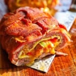 A close-up view of a smoked Western omelette fatty that has been cut in half revealing the melty cheddar cheese, sautéed vegetables, cooked eggs, and juicy sausage, all wrapped in a seasoned bacon weave.